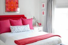 a glam neutral bedroom with a red upholstered bed, neutral and red bedding, a grey upholstered bench and a crystal chandelier