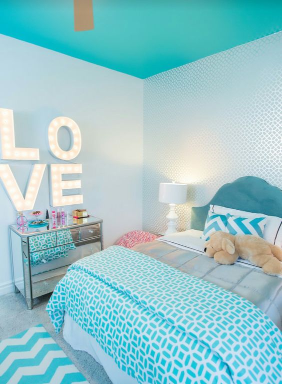 a kid's bedroom with a turquoise ceiling, a turquoise bed with bright printed bedding, a mirror dresser, marquee letters