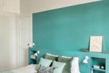 a lovely contemporary bedroom with a turquoise accent wall and storage niches, a bed with light green and neutral bedding and a pendant lamp