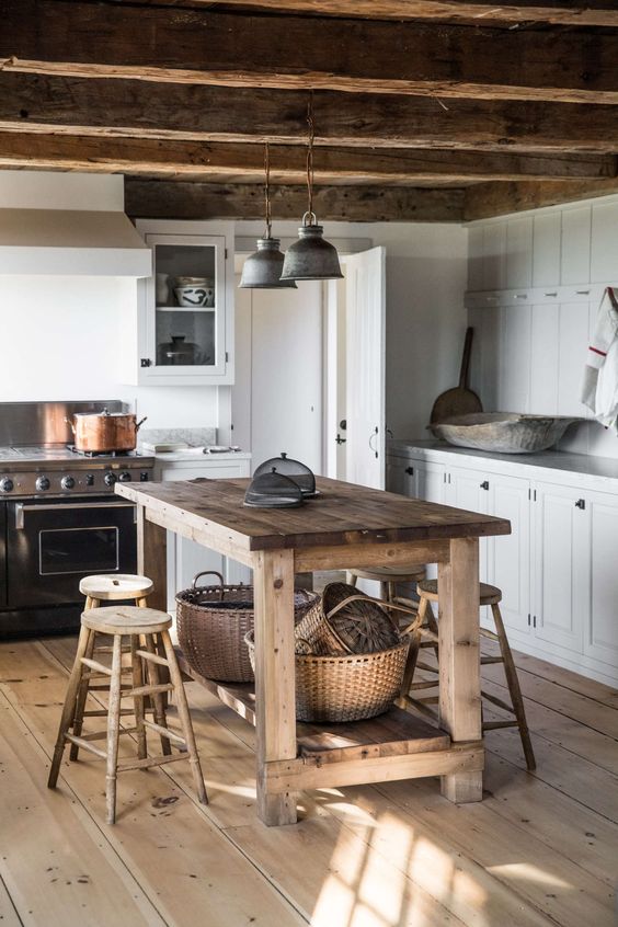 a lovely farmhouse kitchen with white cabinets, stone countertops, wooden beams on the ceiling, a vintage stained kitchen island and stools