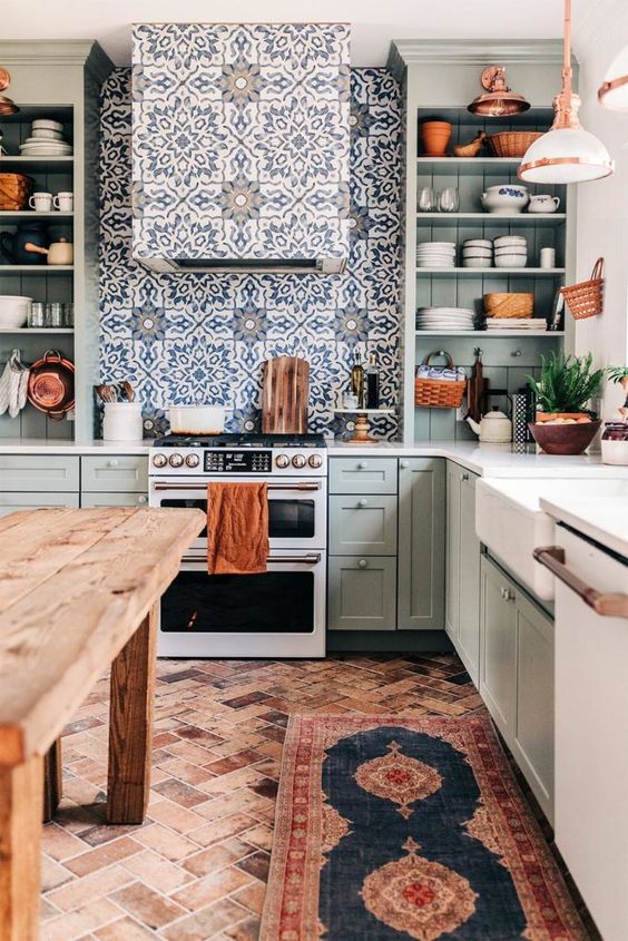 a lovely olive green kitchen with shaker style cabinets, open shelves, a beautiful tile backsplash and hood, a vintage wooden kitchen island