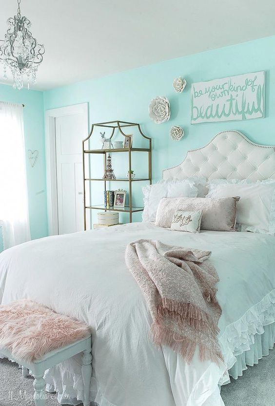 a lovely turquoise teen girl bedroom with a refined upholstered bed and pastel bedding, a brass storage unit and some art