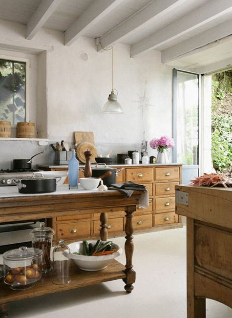 a lovely vintage kitchen with stained cabinets, white wooden beams on the ceiling, a stained kitchen island as a dining table