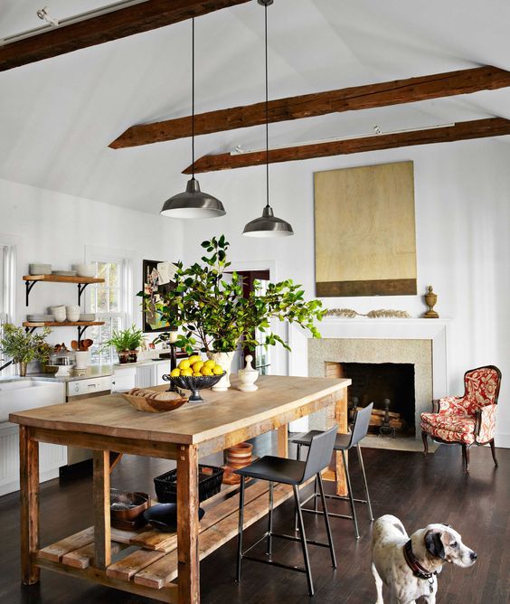 a lovely white farmhouse kitchen with open shelves, a fireplace, a large wooden table that doubles as a kitchen island and black stools