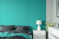 a minimalist bedroom with a turquoise paneled accent wall, a white bed with grey bedding, a white dresser and a nightstand