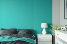 a minimalist bedroom with a turquoise paneled accent wall, a white bed with grey bedding, a white dresser and a nightstand