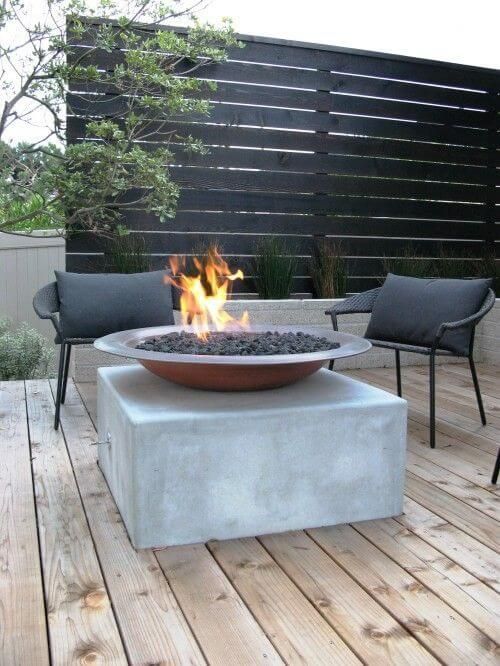 a minimalist summer deck with a concrete cube, a fire pit, dark metal chairs and a screen for privacy