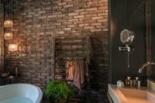 a moody and dark bathroom with brick walls, a wooden floor, large modern fixtures and cool pendant lamps