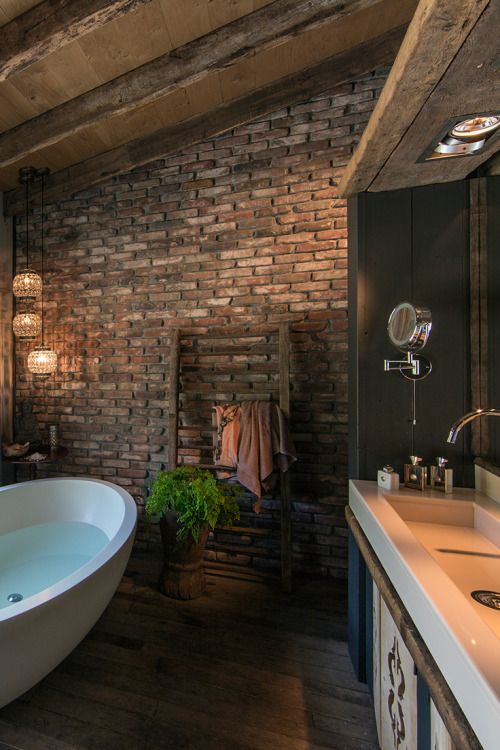 a moody and dark bathroom with brick walls, a wooden floor, large modern fixtures and cool pendant lamps