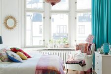 a neutral bedroom with a bay window, neutral furniture, colorful textiles, a pink pendant lamp and turquoise curtains