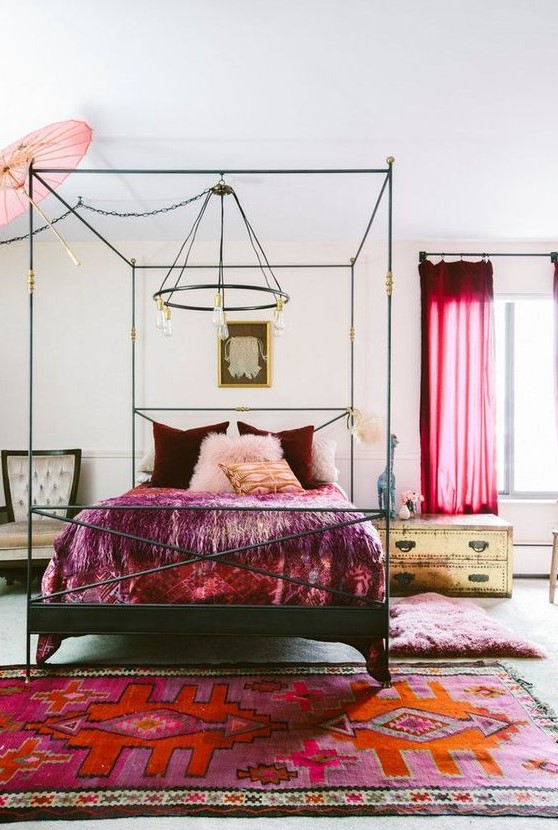 a neutral eclectic bedroom done with catchy gold and black furniture, bold red curtains, burgundy and red bedding and a colorful rug