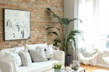 a neutral living room with potted greenery, black touches and an exposed brick wall for more drama