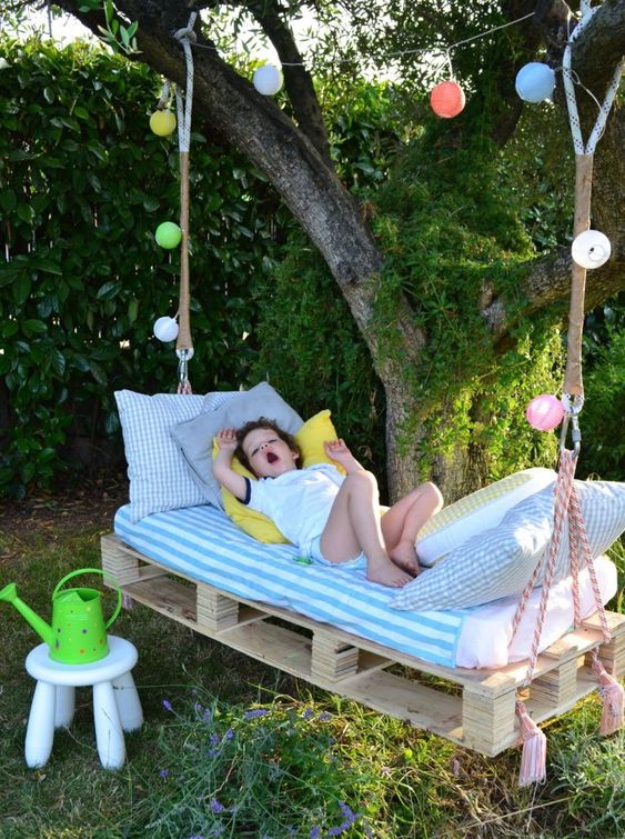 a pallet hanging bed on ropes with colorful lights and cool striped bedding will be loved by your kids