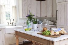 a pretty cottage whitewashed kitchen with white stone countertops, a neutral table that doubles as a kitchen island and a metal pendant lamp