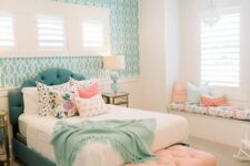 a pretty mid-century modern bedroom with a turquoise accent wall, a teal bed with colorful bedding, a peachy pink ottoman and a windowsill bench