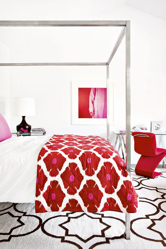 a pure white bedroom spruced up with color, with a canopy bed with colorful bedding, a glass desk, a red chair, a bold artwork