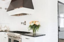 a purely white kitchen with white brick walls and a dark hood that stands out in a neutral space