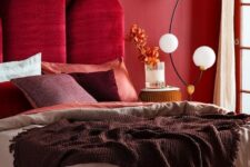 a refined bedroom with a red accent wall, a bold burgundy velvet upholstered headboard and a catchy floor lamp