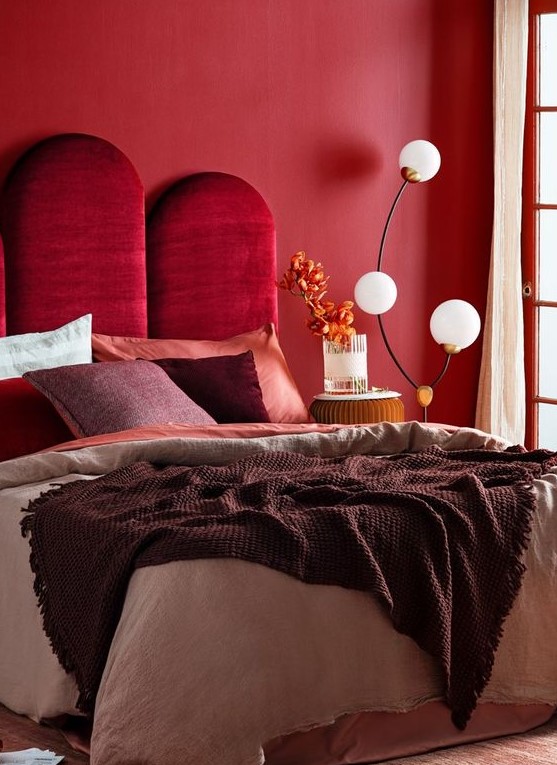 a refined bedroom with a red accent wall, a bold burgundy velvet upholstered headboard and a catchy floor lamp