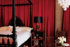 a refined bedroom with red curtains, a heavy black bed and black nightstands, a carved chair, some chandeliers