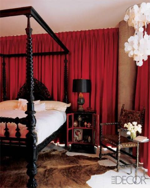 a refined bedroom with red curtains, a heavy black bed and black nightstands, a carved chair, some chandeliers