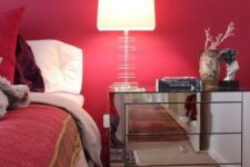 a refined mid-century modern bedroom with a red accent wall, bold red and burgundy bedding, a printed rug and a mirror nightstand with a chic lamp