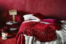 a refined red bedroom with a red plaster wall, a red rug, neutral, fuchsia and red bedding and a chic lamp