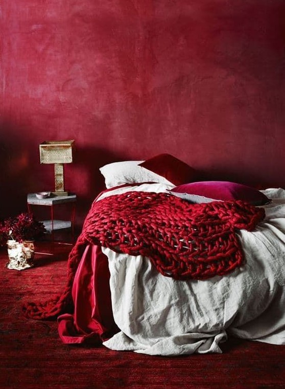 a refined red bedroom with a red plaster wall, a red rug, neutral, fuchsia and red bedding and a chic lamp