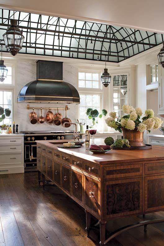 a refined vintage kitchen with shaker style cabinets, a black hood, a vintage table with plenty of storage, vintage metal lamps