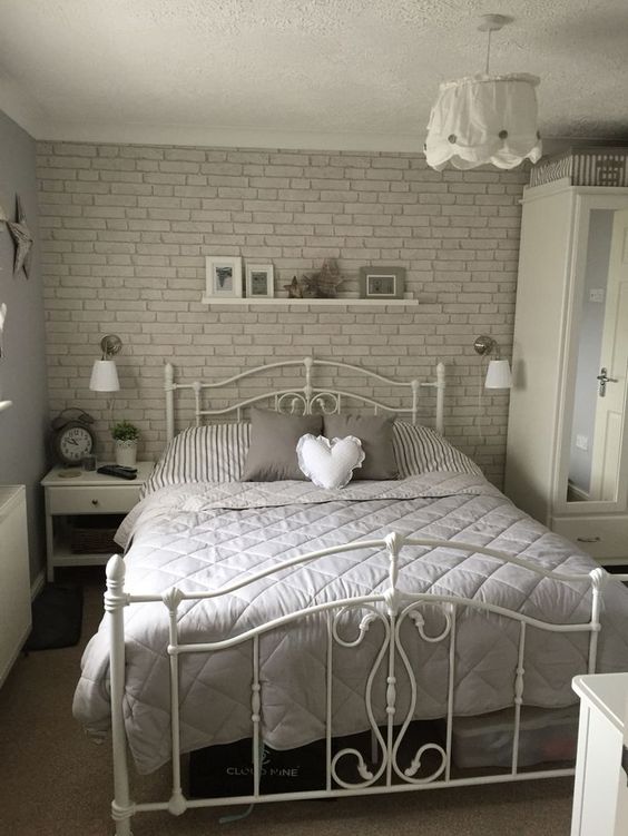 a romantic bedroom with a fau grey brick wall, a forged bed, some chic white furniture and lamps