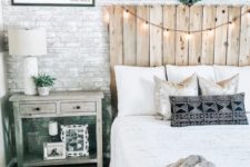 a rustic bedroom with a white fake brick wall, a reclaimed wood bed, lights and vintage furniture