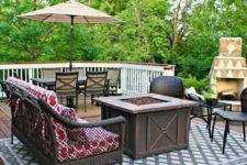 a rustic deck with dark wicker furniture, an umbrella with a dining zone, a fire pit in the center and a fireplace