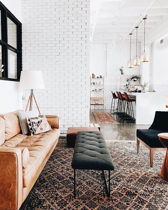 a serene living room withwhite brick walls, brown and amber leather furniture and an upholstered bench