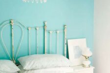 a shabby chic bedroom with a turquoise accent wall, a gorgeous crystal chandelier, a metal bed with white bedding