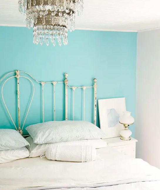 a shabby chic bedroom with a turquoise accent wall, a gorgeous crystal chandelier, a metal bed with white bedding