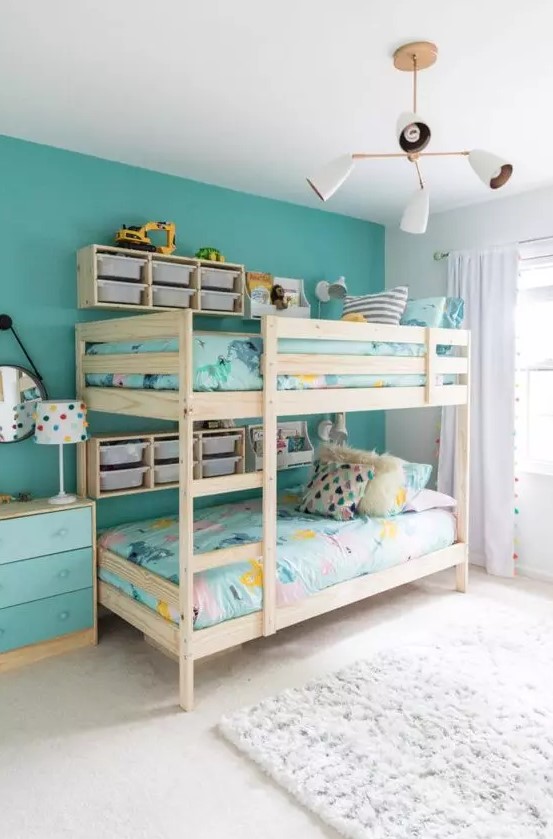 a shared kids' room with a turquoise accent wall, a wooden bunk bed with bright bedding, an ombre turquoise dresser