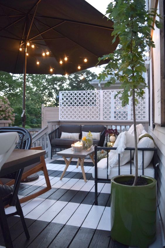 a striped deck with a dining and sitting space, some potted greenery, trees and blooms plus candle lanterns