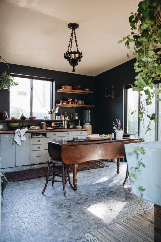 a stylish kitchen with black walls, white shabby chic cabinets, butcherblock countertops, a stained folding table as a kitchen island