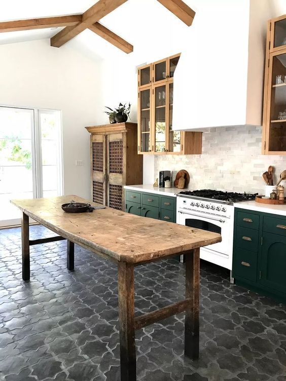a stylish two-tone kitchen with a large hood, wooden beams on the ceiling, a tiled floor and a vintage wooden table