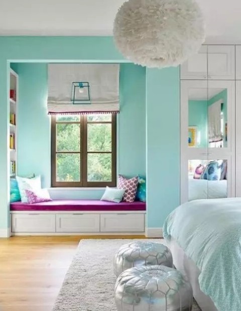 a turquoise bedroom with a window reading nook with built in shelves, a bed with turquoise and white bedding and silver poufs