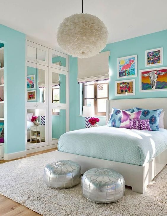 a turquoise teen girl bedroom with a built in closet with mirror doors, a neutral bed with colorful bedding, silver poufs and a fluffy pendant lamp