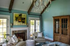 a vintage attic bedroom with wooden beams, turquoise walls, a bed with light blue bedding, a stained bookcase, a fireplace and some seating furntiure