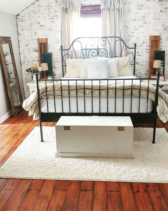 a vintage bedroom with a faux whitewashed brick wall that adds texture to the space and a rich stained wooden floor