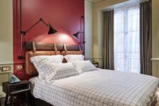 a vintage-inspired bedroom with a red accent wall, vintage furniture and metal sconces, windowpane bedding and simple curtains