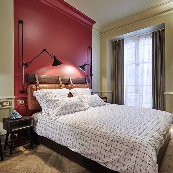 a vintage-inspired bedroom with a red accent wall, vintage furniture and metal sconces, windowpane bedding and simple curtains