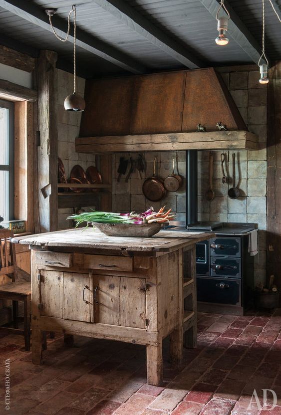 a vintage kitchen with black cabinets, an aged metal hood, a vintage wooden kitchen island and pendant lamps