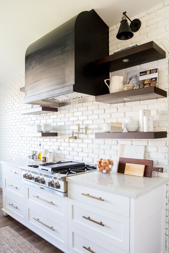 a vintage kitchen with white cabinets, copper hardware and a whiet faux brick wall that makes the hood stand out