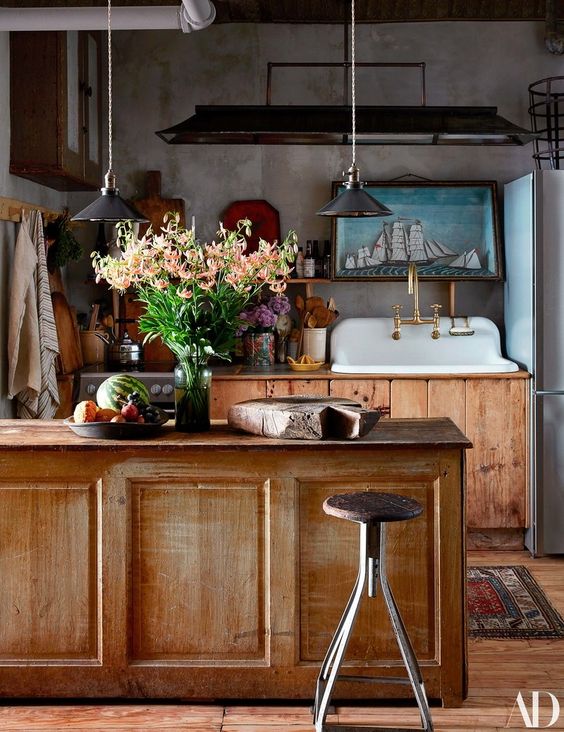 a vintage rustic kitchen with stained cabinets, a matching vintage kitchen island, pendant lamps and a dark metal hood