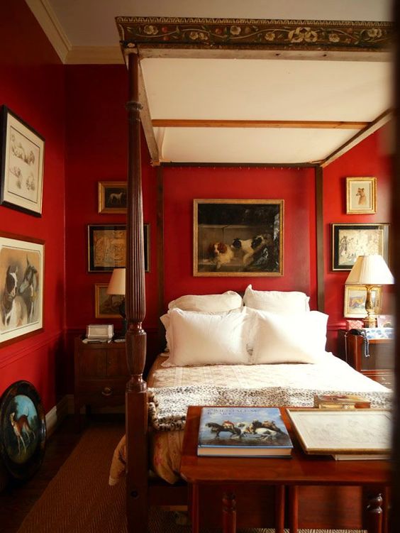 a vintgae inspired bold red bedroom with a refined cnaopy bed, vintage artworks, nightstands and table lamps and a bench with books