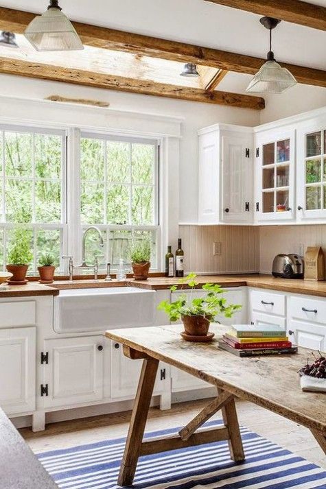 a welcoming farmhouse kitchen with white shaker cabinets, wooden beams on the ceiling, a wooden kitchen island that is a table